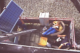 part of installation team taking a break while another member starts carrying a solar panel up the ladder towards the flat roof